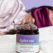 Jar labeled 'vena lights out' gummy supplement on a bed with a blurred sleeping person in the background.