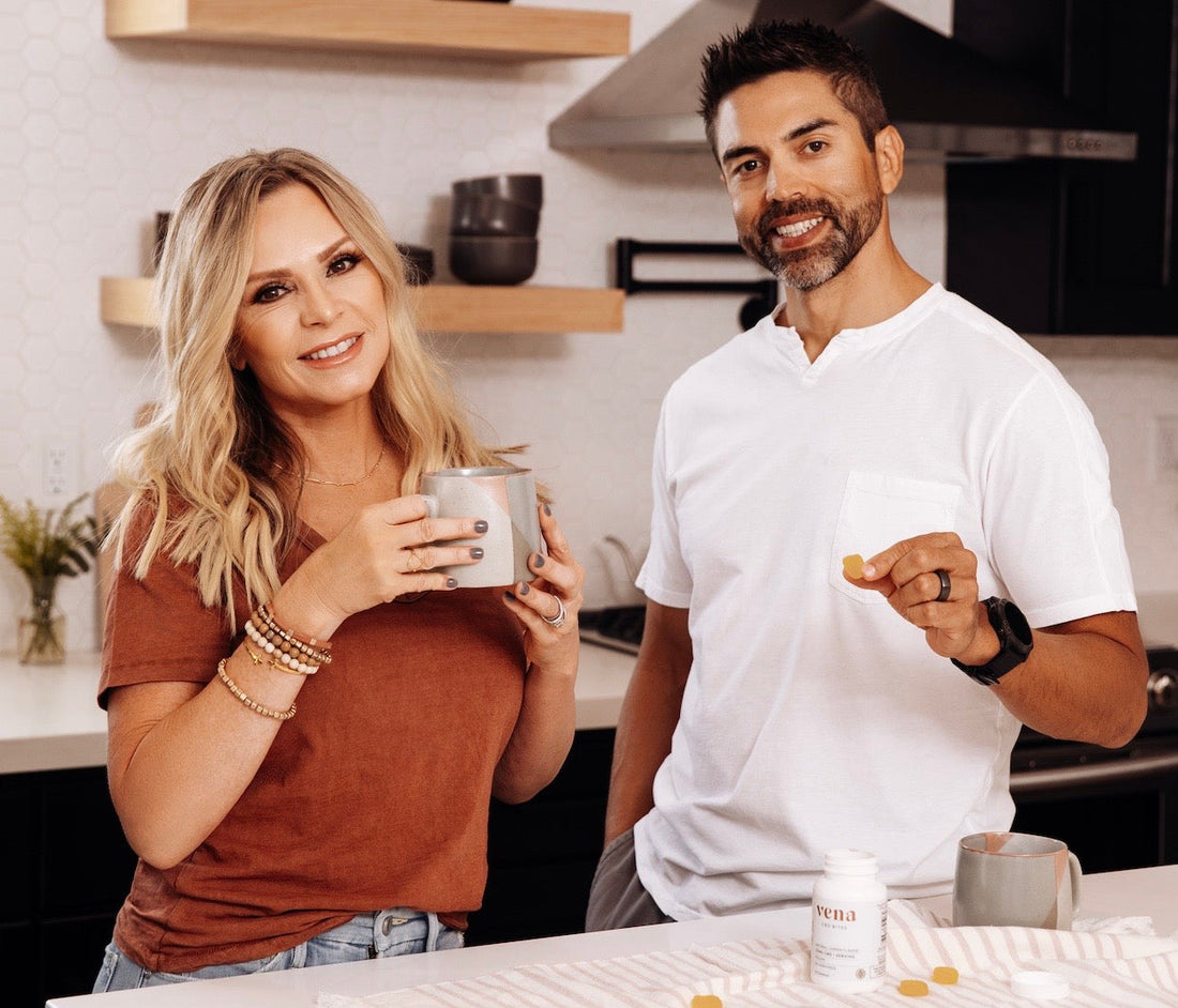 Two people smiling in a kitchen holding mugs; a vena supplement bottle and a gummy on the counter.