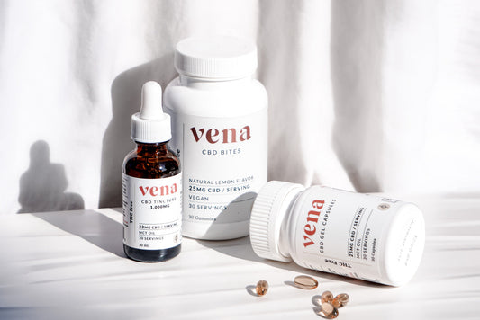 Vena CBD amber tincture with white dropper, two white 'vena' supplement bottles, and several golden softgel capsules.