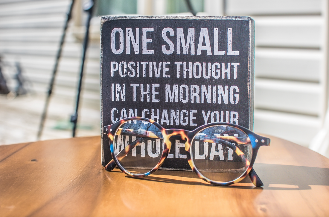 ONE SMALL POSITIVE THOUGHT IN THE MORNING CAN CHANGE YOUR WHOLE DAY — tortoiseshell glasses resting on a wooden table.