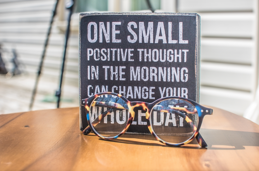 ONE SMALL POSITIVE THOUGHT IN THE MORNING CAN CHANGE YOUR WHOLE DAY — tortoiseshell glasses resting on a wooden table.
