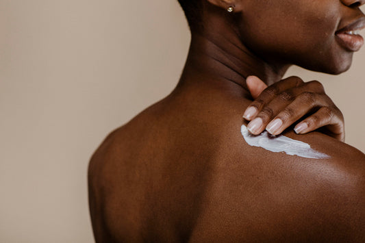 Close-up of a person applying white cream to their shoulder with manicured nails.